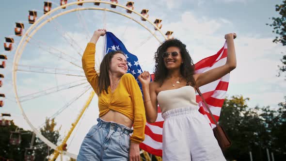 Young Mixed Race Girls in Sunglasses are Smiling and Dancing Holding Flag of USA and Waving It