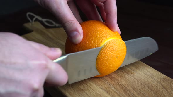 Man Slicing Raw Orange with Kitchen Knife on Wooden Cutting Board