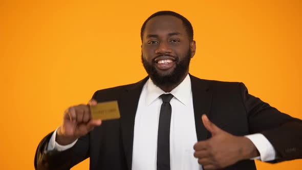 Fashionable Smiling Black Man in Formalwear Showing Gold Card and Thumbs-Up