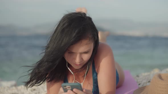 Lifestyle Girl Lying on the Beach and Listening to Music on Headphones