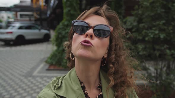 Young Woman with Long Curly Hair in Sunglasses Makes a Selfie on the Street