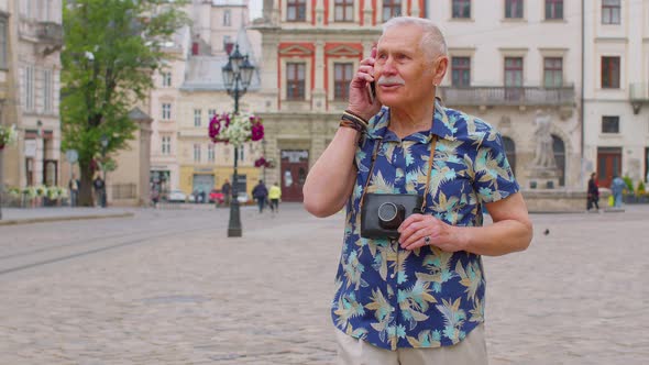 Senior Old Tourist Man in Stylish Clothes Talking on Mobile Phone While Walking on City Street