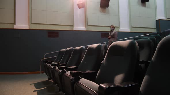Woman in Mask Sits on Chair in Front Row of Empty Auditorium