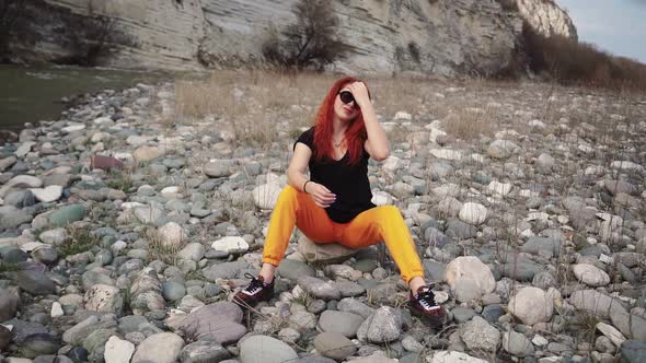 Fashionable Woman in Sunglasses Sitting Resting on Rocky Bank Mountain River