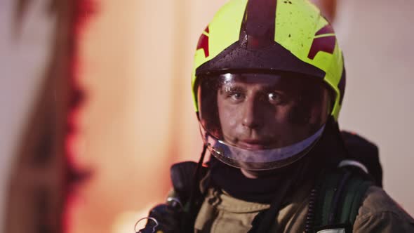 Potrait of Young Firefighter in Full Uniform in Front of Burning House