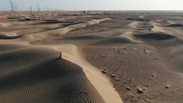 Young Woman is Sitting on Top of a Sand Dune and Throwing Sand Sunset