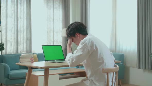 Side View Of Asian Man Student Being Tired While Looking At Green Screen Computer At Home