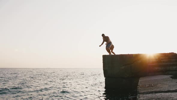 Young Woman and Man Jumping From a Pier Into the Sea and Doing Tricks During Beautiful Sunrise Slow