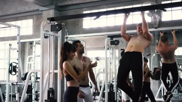Friends Cheering Man Practicing Chin Ups Exercise on Bars at the Gym