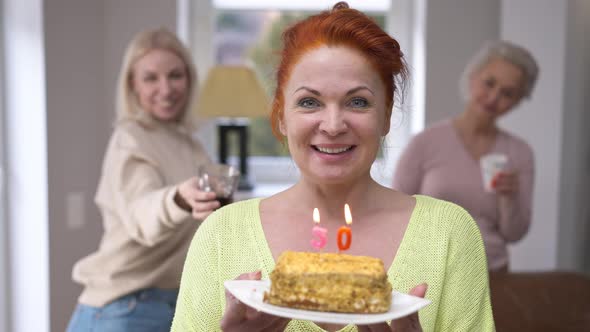 Front View Happy Woman Blowing Out Candles on Cake Making Wish Looking at Camera Smiling