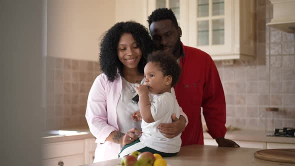 Carefree Adorable African American Toddler Boy Eating Children Food From Tube As Satisfied Father