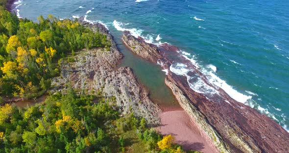 Aerial Up Close on Coast of Small Island with Lake Waves and Fall Trees