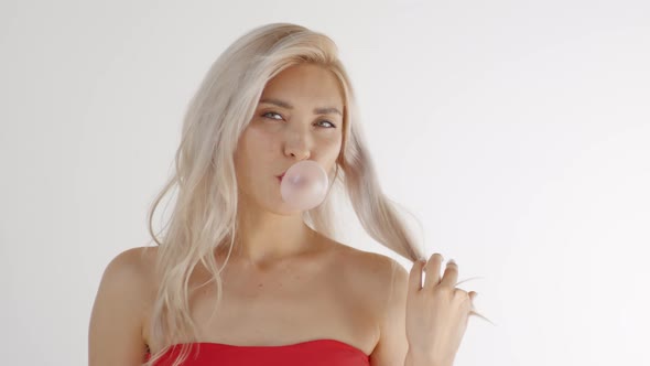 Lovely Blonde Woman Chewing Gum and Blowing Bubbles in Studio