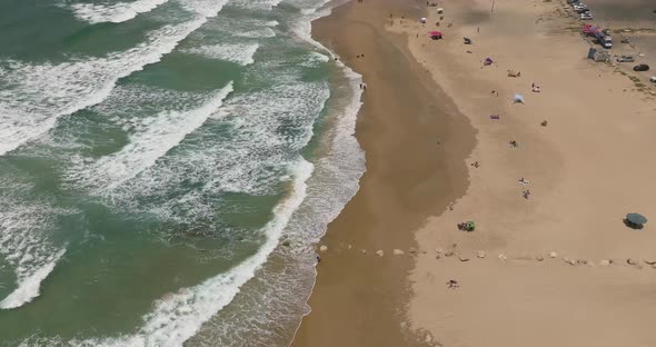 Summer day at a local beach with people relaxing under umbrellas and waves breaking.