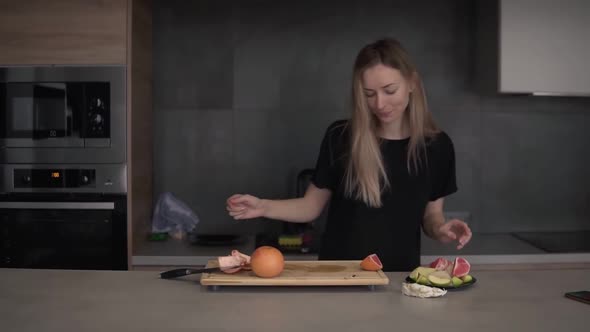 Positive Woman Cleaning Grapefruit Peel on Chopping Board at Kitchen and Dancing