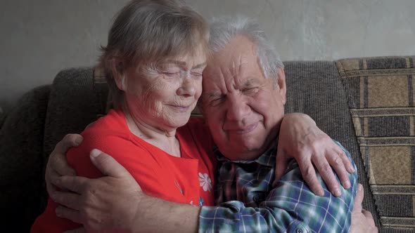 Old Elderly Couple Hugging Sitting On Couch In House