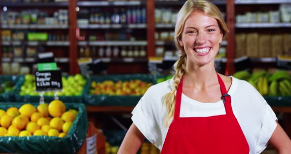 Smiling female staff standing with hands on hip in grocery section