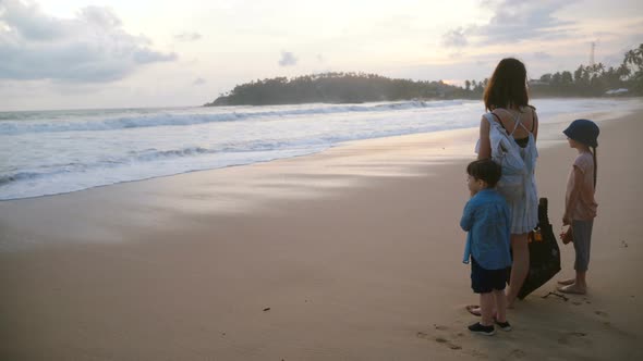 Back View Happy Young Mother Together with Two Kids Watching Incredible Atmospheric Sunset at Exotic
