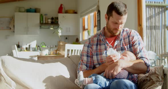 Front view of mid adult caucasian father feeding milk his baby from bottle in a comfortable home 4k