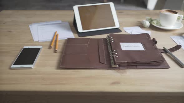 brown wood table work space area desktop leather case notepad journal tablet phone watch coffee cup