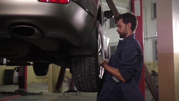 Skillful Auto Mechanic Putting Wheel on Raised Car