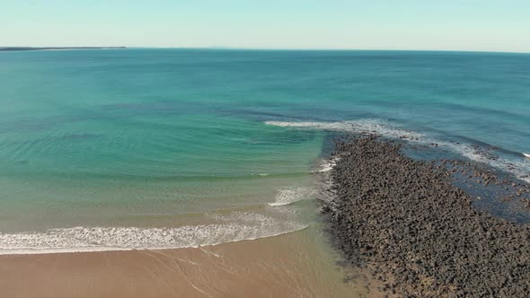 AERIAL DOLLY BACK Black Volcanic Rocks Along A Sandy Beach