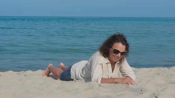 A happy woman on vacation is lying on the sand.