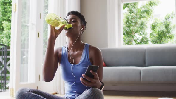 African american woman drinking water and using smartphone at home