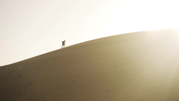 Man Walking Up Sand Dune In Desert