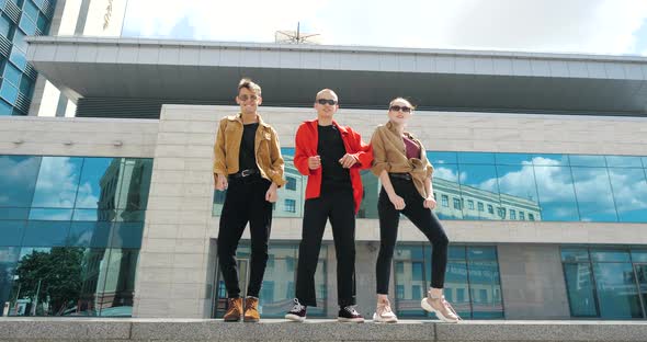 Three Teenage Caucasian Millennials Standing Together Outdoors Against Background of Blue Business