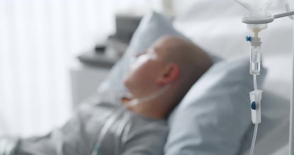 Focus on Intravenous Drip with Sick Kid Lying in Hospital Bed on Background