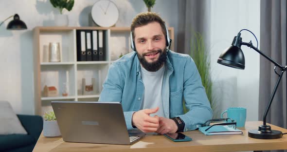 Bearded Guy in Headset Showing Sign Like Into Camera Sitting at the Desk in Home Office