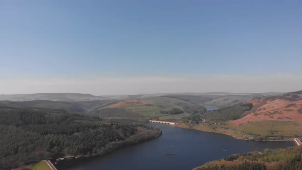 Drone travelling rising with Lady Bower Reservoir in view from Bamford Edge in the Peak District sho