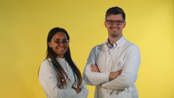 Mixed-race Male and Female Doctors Smiling To the Camera on Yellow Background.