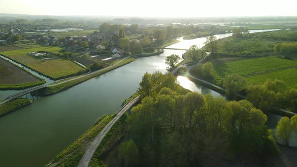 Aerial view in the sunset of a river in Clairmarais, France. We see a village and a bridge in the di