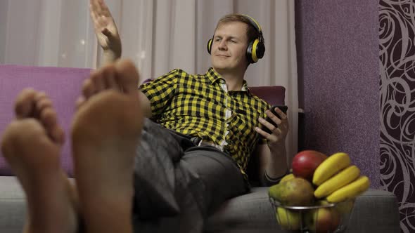 Man Lying on the Sofa Listens Music with Wireless Headphones and Dances