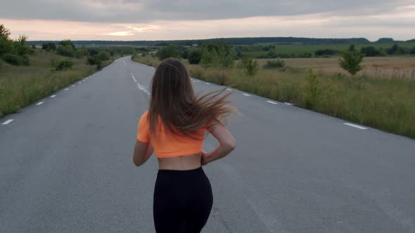 Rear View of Sporty Girl with Long Hair Jogging Marathon on Road at Nature