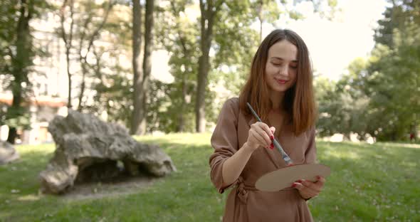 Girl Artist Stands in the Park with a Palette in Hand and Smiles