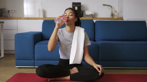 African American Woman Drinking Water After Workout at Home on Yoga Mat