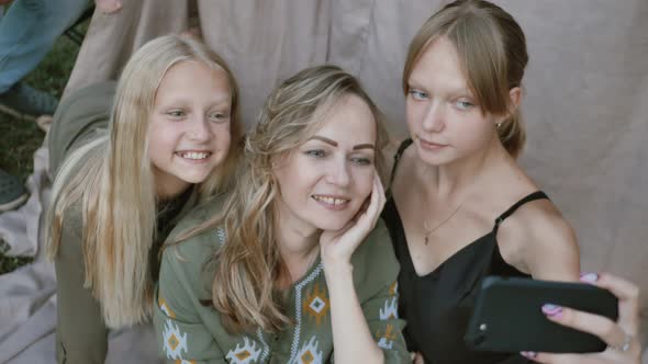 Close up of smiling mother with daughters makes funny selfies on the smartphone, grimacing