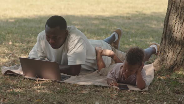 Man with Son Video Conferencing on Laptop in Park