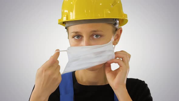 Female Construction Worker in Safety Helmet Putting Medical Mask on on Gradient Background