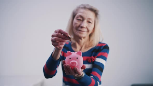 Elderly Retired Woman Inserting Coins Into the Piggy Bank