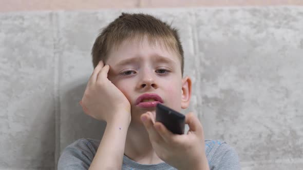 Portrait of caucasian boy 8 years old with tv remote control bored watching tv programs at home.Chil