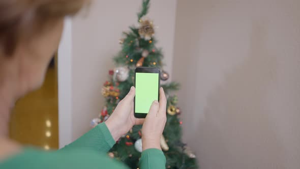 Old Woman Holding Mobile Phone With Green Screen Taking Photos Of Christmas Tree In The Corner Of