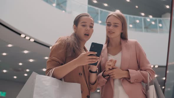 Happy Women with Shopping Bags Looking at Mobile Phone