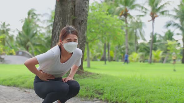 Asian sport woman wear mask feels pain on stomach after running during pandemic in public park.