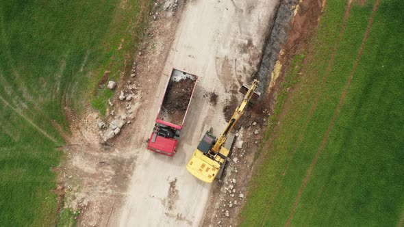 Top View Yellow Excavator Picks Up Land From the Field and Loads It Onto a Red Truck