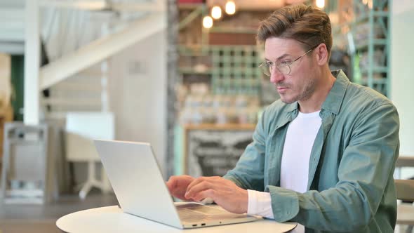 Tired Middle Aged Man with Laptop Having Neck Pain in Cafe