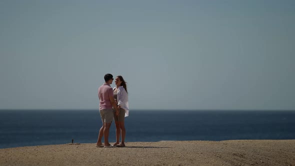 a Woman with Long Hair in a White Shirt and a Man in a Pink Tshirt are Standing and Holding Hands on